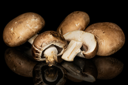 Group of four whole one half of fresh brown mushroom champignon isolated on black glass