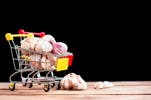 Toy shopping trolley with cloves of garlic. Yellow background and copyspace for text.