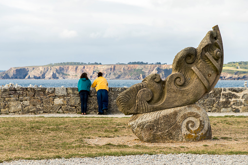 Camaret-sur-Mer, France. Two women looking at the coast from the Sillon with a sculpture in the foreground