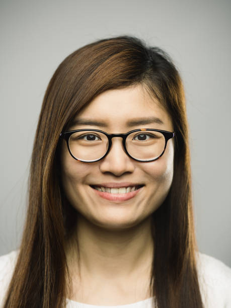 Real chinese young woman with happy expression Close up portrait of asian young woman with happy expression against gray white background. Vertical shot of chinese real people smiling in studio with long brown hair and eyeglasses. Photography from a DSLR camera. Sharp focus on eyes. passport photos stock pictures, royalty-free photos & images