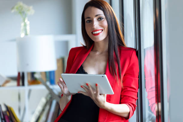 istock Pretty young businesswoman looking at camera while using her digital tablet in the office. 1181864283