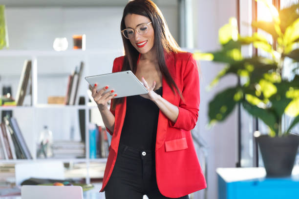 istock Pretty young businesswoman using her digital tablet while standing next to the window in the office. 1181864353