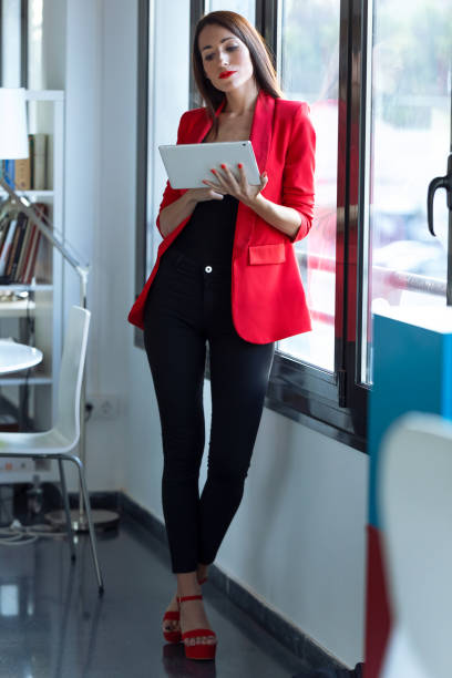 istock Pretty young businesswoman using her digital tablet while standing next to the window in the office. 1181864392
