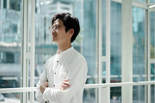 Casual business portrait of a young Asian man standing by the window. Looks like a CEO or engineer.