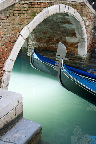 gondole a venezia sotto un ponte con luce - venice italy gondola italian culture italy foto e immagini stock