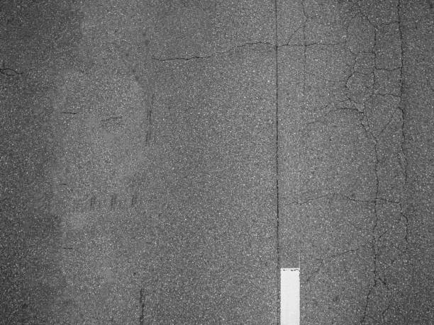 Top view or directly above, abstract black and white tone background of gradient rough and cracked pattern of asphalt street or road texture with white line.