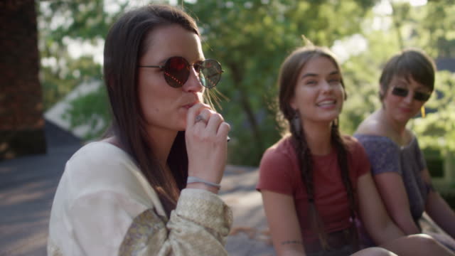 A group of hipster woman hang out on the roof of a house, one of the vapes an electronic cigarette