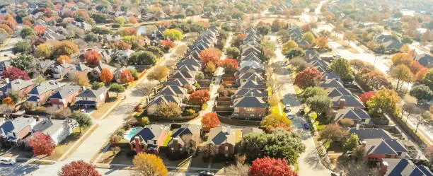 New development neighborhood near Dallas, Texas with colorful orange autumn leaves. Row of two story single family dwelling with large backyard, swimming pool, attached garage and wooden fence garden