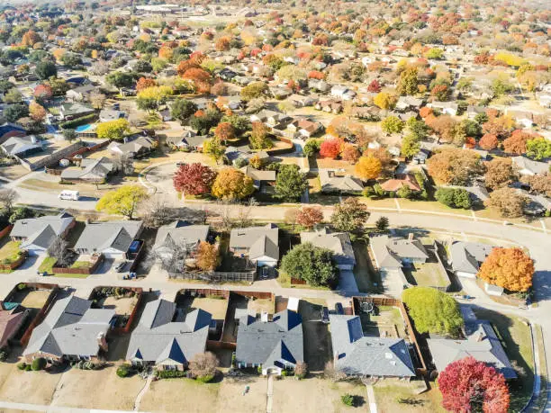 New development neighborhood near Dallas, Texas with colorful orange autumn leaves. Row of two story single family dwelling with large backyard, swimming pool, attached garage and wooden fence garden