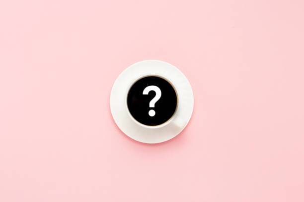 istock White cup on a saucer, black coffee, pink background. Question mark. Flat lay, top view 1181890949
