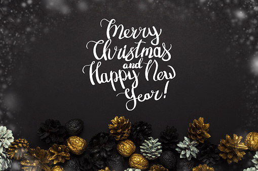 Pine cones and nuts painted in golden, black, white colors on a black background. Added text Happy New Year and Merry Christmas. Flat lay, top view.