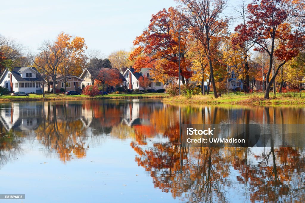 Beautiful autumn Midwest nature background. Fall view of private houses neighborhood with classic american middle class homes and colorful trees along a pond reflected in a water. Tenney Park, Madison, WI. Madison - Wisconsin Stock Photo