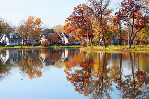 Fall view of private houses neighborhood with classic american middle class homes and colorful trees along a pond reflected in a water. Tenney Park, Madison, WI.