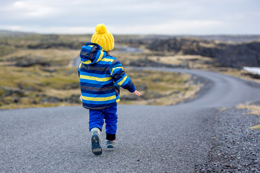 Children, walking on a curved road near ocean in beautiful nature in Snaefellsjokull National Park in Iceland, autumntime
