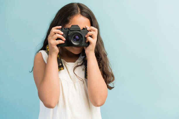 Hispanic Female Photographer Against Plain Background Young Latin girl photographing with digital camera while standing in studio digital camera stock pictures, royalty-free photos & images