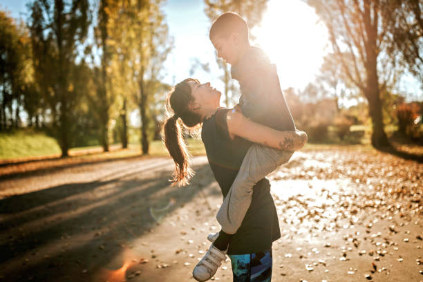 Mother and son on sunny autumn afternoon, woman holding in arms her boy on sunbathed sport field