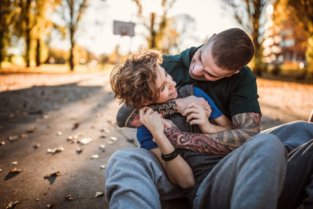 padre tatuato che si abbraccia con il figlio a terra sul campo sportivo - tattoo father family son foto e immagini stock