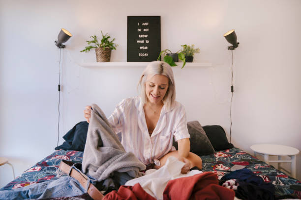 mujer con la cama llena de ropa tratando de preparar la maleta de vacaciones con ropa de temporada. - plegar fotografías e imágenes de stock