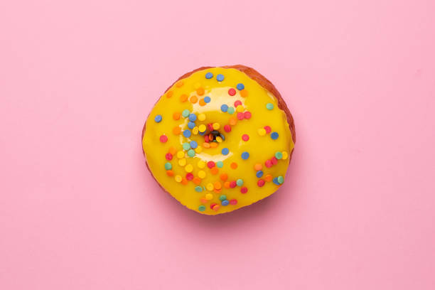 istock Sweet yellow donut with sprinkle on a pink background flat lay 1181917797