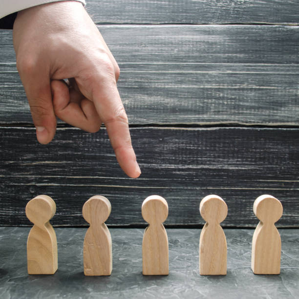 A businessman's hand points to a wooden human figure. Hiring and volnenie employees, pressure, violation of employee rights. The concept of the search for workers, management of human resources. la mano de un hombre de negocios apunta a una figura humana de madera. contratación y volnenie empleados, presión, violación de los derechos de los empleados. el concepto de la búsqueda de trabajadores, la gestión de los recursos humanos.