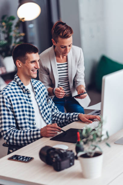 desenhador gráfico que trabalha no computador e que fala com colega - casual teamwork journalist editor - fotografias e filmes do acervo