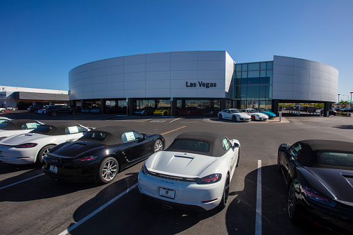 Porsche of Las Vegas. Rows of the luxury sports cars and SUV's can be seen lined up outside of the modern dealership building.