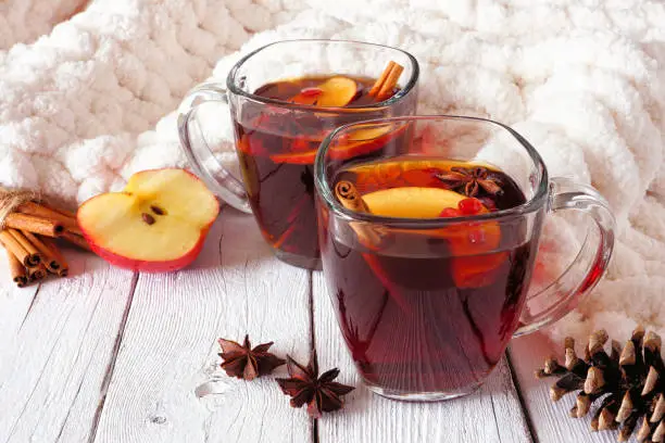 Autumn spiced tea with apples and pomegranates. Side view on a white wood background with blanket. Cozy fall or winter theme.