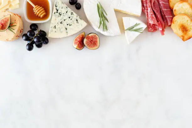 Photo of Assorted cheeses and meat appetizers, overhead view top border on a white marble background with copy space