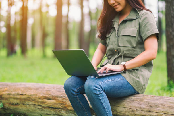 istock woman using and typing on laptop keyboard while sitting on a log in the park 1181966839