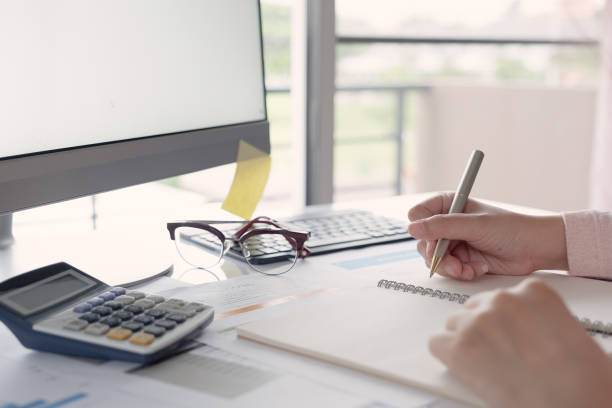 istock Young business woman sitting at table and taking notes in notebook.On table is laptop. 1181975271