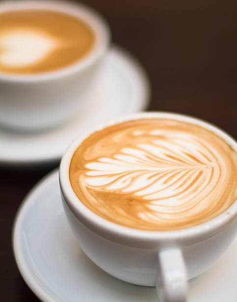cappuccino em uma xícara, com decoração em espuma e bokeh de fundo - latté cafe froth art cup - fotografias e filmes do acervo