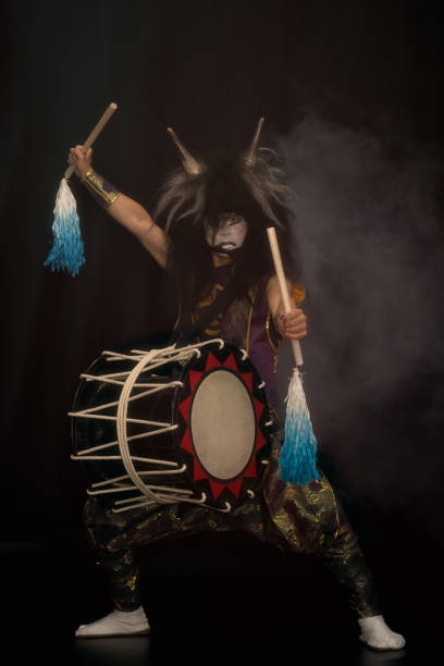 demone della mitologia giapponese. ritratto a figura intera di un batterista artista taiko in una parrucca con corna e tamburo make-up sul palco su uno sfondo scuro. - lenght foto e immagini stock