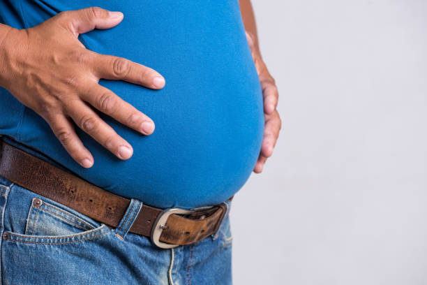 homem adulto do excesso de peso ou gordo em calças de brim muito apertadas em um fundo cinzento. saúde, conceito de medicina. - overweight - fotografias e filmes do acervo