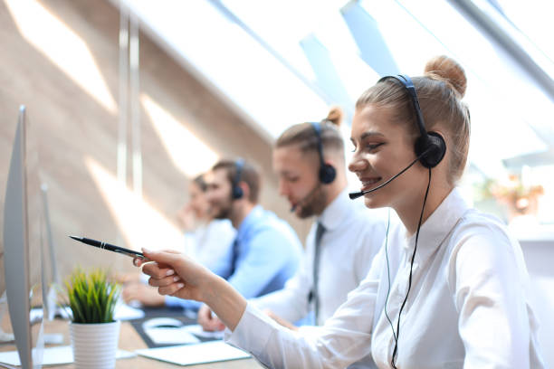 istock Female customer support operator with headset and smiling accompanied by her team. 1181989212