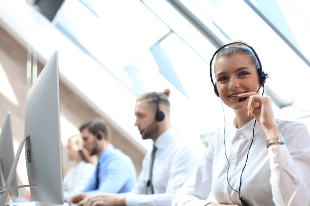 istock Female customer support operator with headset and smiling accompanied by her team. 1181989321