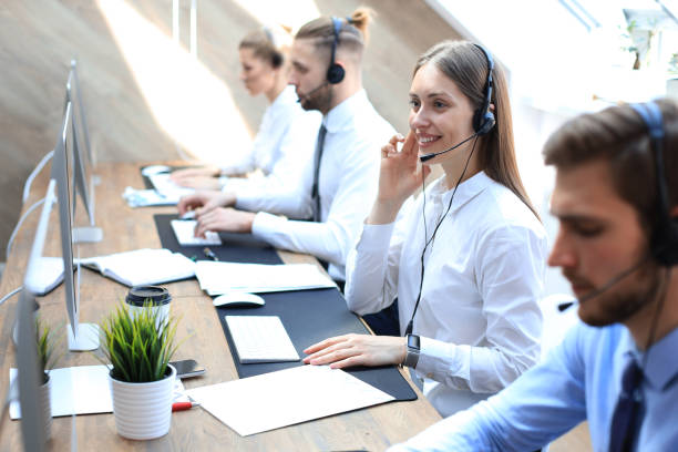 istock Female customer support operator with headset and smiling accompanied by her team. 1181989337