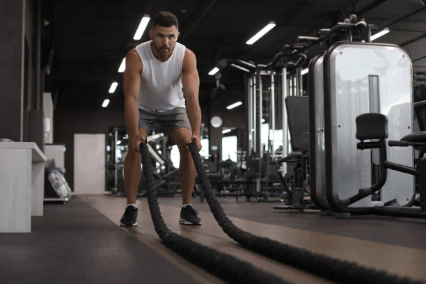 istock Athletic young man with battle rope doing exercise in functional training fitness gym. 1181991147