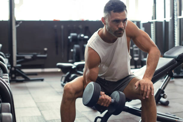 istock Fit and muscular man doing biceps workouts with dumbbells in gym, copy space. 1181991287