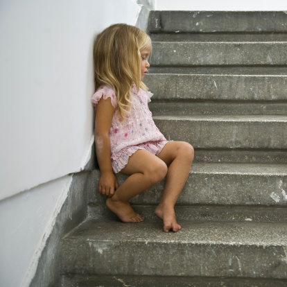 Little abandoned child sitting alone on staircase, barefoot