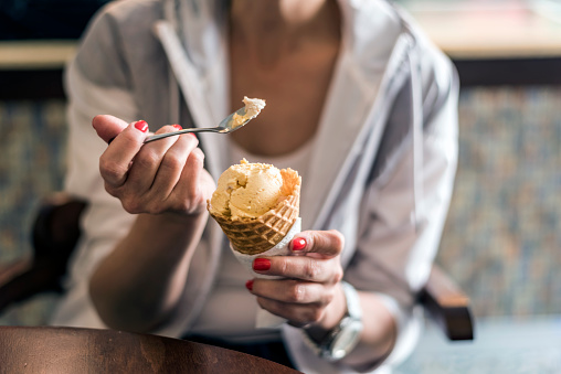 Girl holding spoon with ice cream cone, eating ice-cream in cafe, hands holding ice-cream