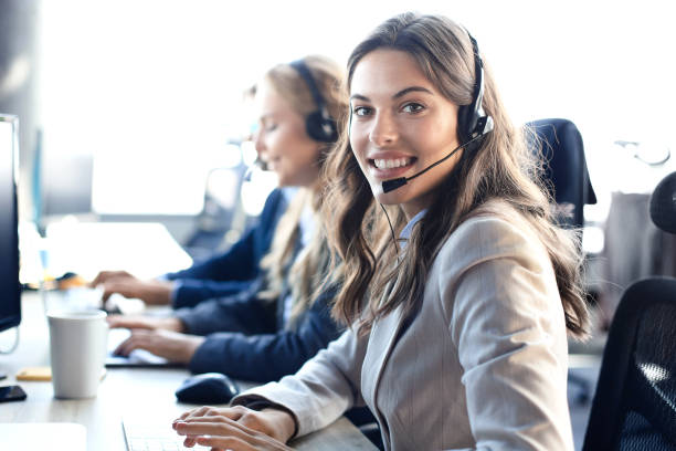 istock Female customer support operator with headset and smiling, with collegues at background. 1181997009