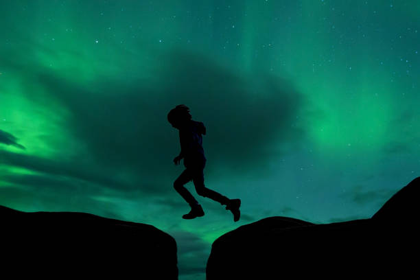 silhouette del bambino in età prescolare, saltando sul vuoto sullo sfondo del cielo dell'aurora boreale - star shape sky star aurora borealis foto e immagini stock