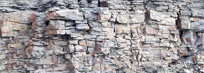 Rock cliff face background. Dangerous vertical wall with protruding crumbling layered stone blocks in quarry for the extraction of wild stone. Abstract texture for stone mining industry.