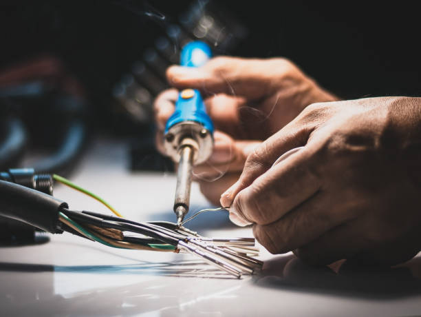 電気技師は、ワイヤを金属ピンに接続するためにはんだ付け鉄を使用しています。 - はんだごて ストックフォトと画像
