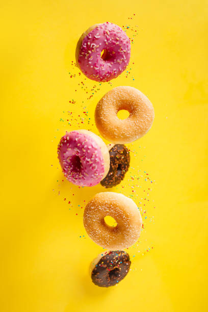 various decorated doughnuts with sprinkles in motion falling on yelloy background - candied sugar imagens e fotografias de stock