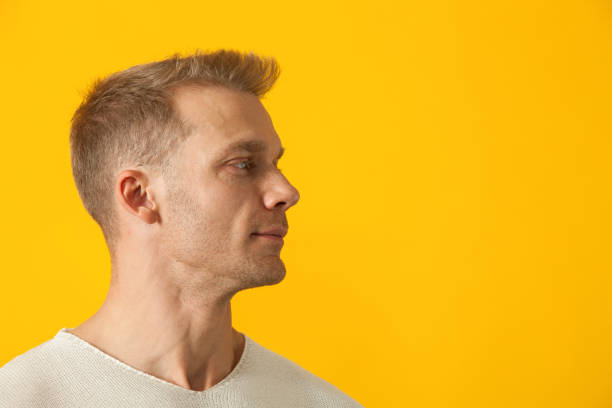 Studio portrait of a 40 year old man in a white sweater on a yellow background stock photo