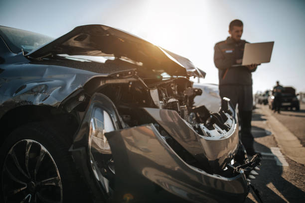 mechanic working on laptop in front of damaged car on parking lot - vehicle wreck imagens e fotografias de stock