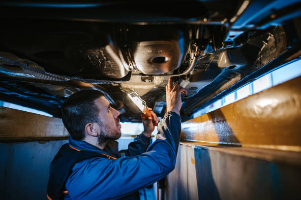 mechaniker, der die unterseite des autos untersucht, während er elektrische lampe hält - maintenance engineer car lamp protective workwear stock-fotos und bilder