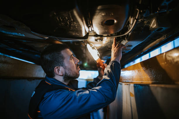 Mechanic examining underside of car while holding electric lamp