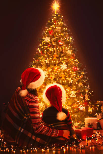 weihnachten familie suchen beleuchtung xmas baum, mutter und kind in roten weihnachtsmann hüte, silvester - christmas family child christmas tree stock-fotos und bilder